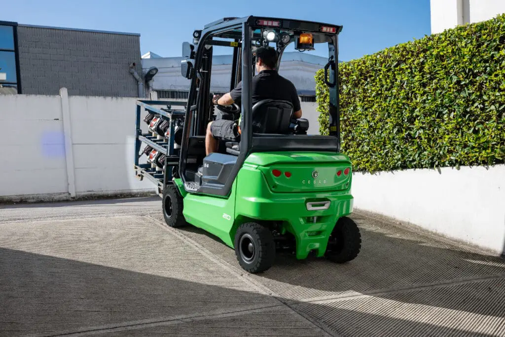 Driver on a green CESAB B4-20 forklift moving a load across a paved driveway outside. - Prince Maasdijk