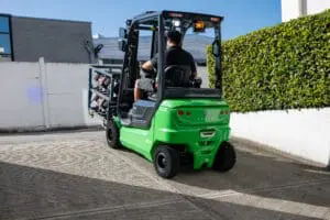 Driver on a green CESAB B4-20 forklift moving a load across a paved driveway outside. - Prince Maasdijk