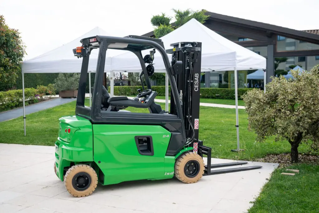 Green CESAB B420 forklift in use in a warehouse full of stacked cardboard, seen from rear view. - Prince Maasdijk