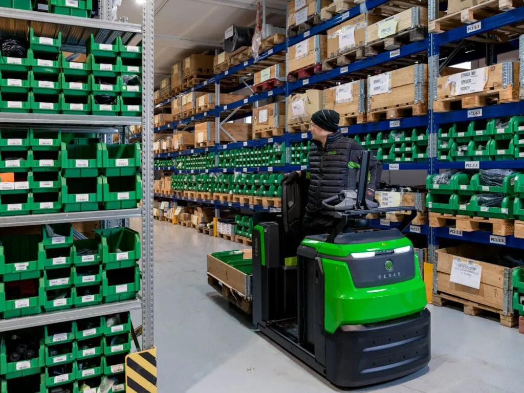 Warehouse employee transports pallet with CESAB O1 electric pallet truck in narrow aisle of parts warehouse | Prins Maasdijk