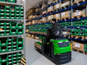 Warehouse employee transports pallet with CESAB O1 electric pallet truck in narrow aisle of parts warehouse | Prins Maasdijk