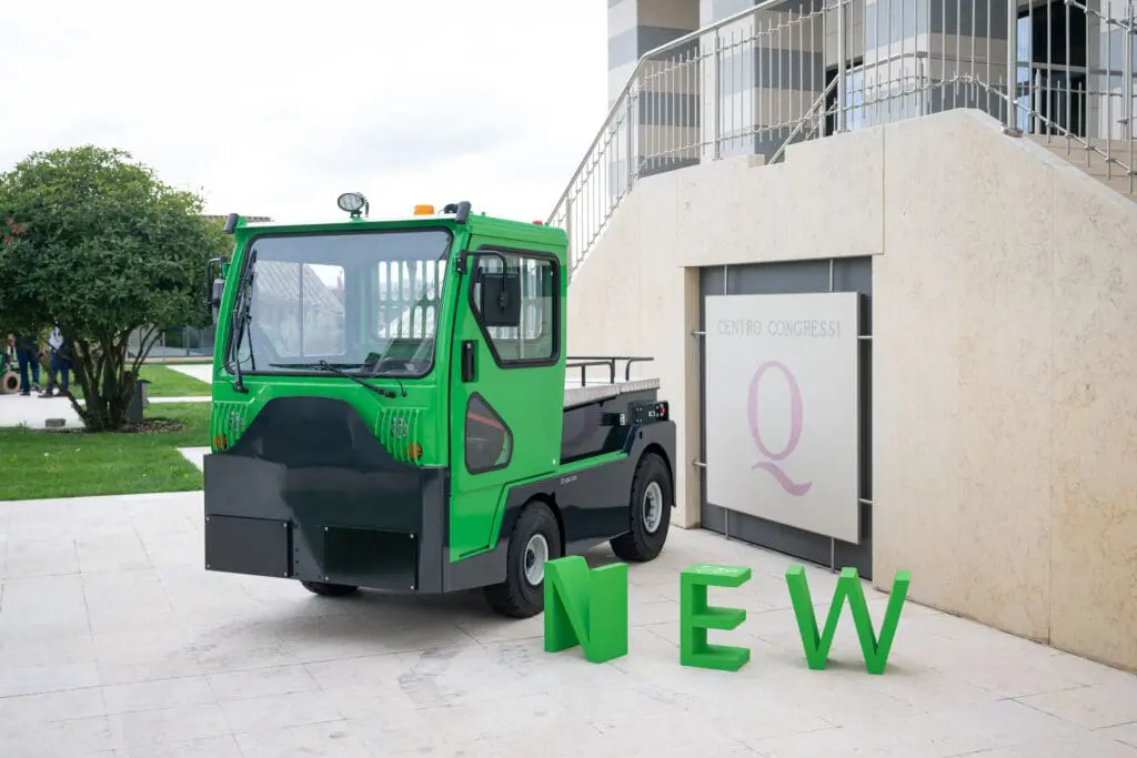 Green electric tractor (Tracto TE252) in front of a convention center with large green "NEW" letters in the foreground. - Prince Maasdijk