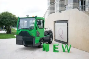 Green electric tractor (Tracto TE252) in front of a convention center with large green "NEW" letters in the foreground. - Prince Maasdijk