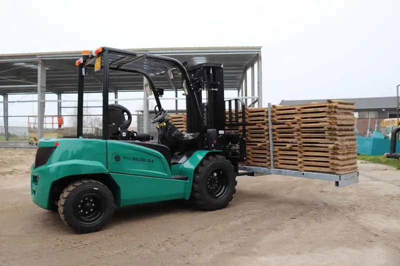 Green Prince Bulldog 25-E electric forklift with a stack of wooden pallets in an outdoor yard, left side view. - Prince Maasdijk