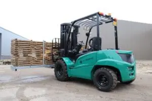 Green Prince Bulldog 25-E electric forklift with a load of wooden pallets outside at an industrial building, right side view. - Prince Maasdijk