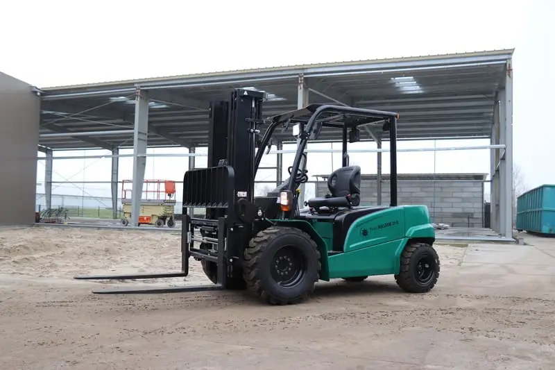 Green Prince Bulldog 25-E electric forklift outside on a sandy lot next to an industrial hall, front view. - Prince Maasdijk