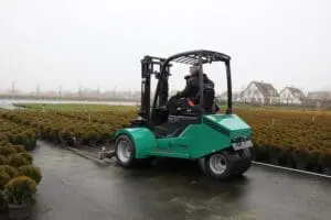 Driver on a green Prins Tiger XXL-E Zero Emission forklift in use on an outdoor nursery of potted plants. - Prince Maasdijk